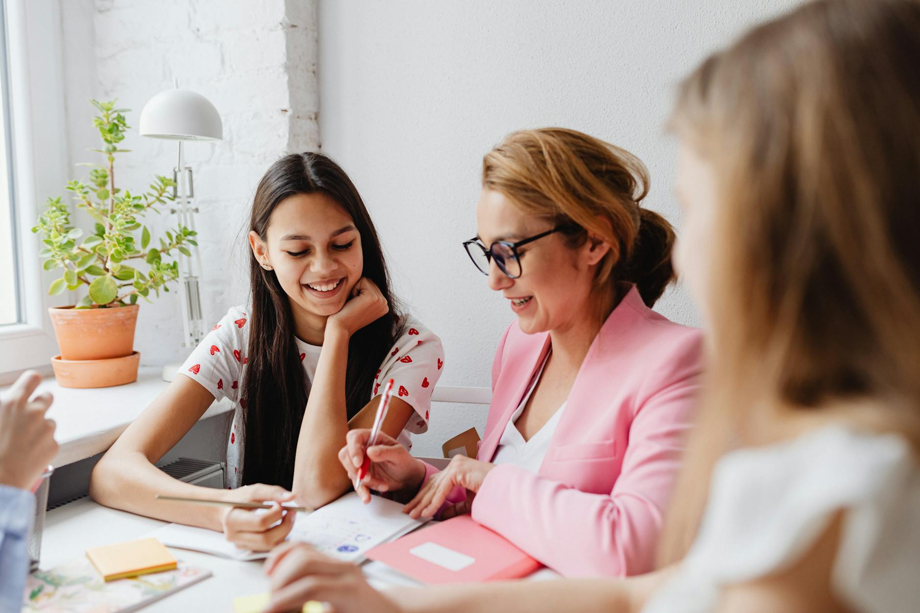 a woman in pink long sleeve shirt holding a pen and notebook beside a young woman
